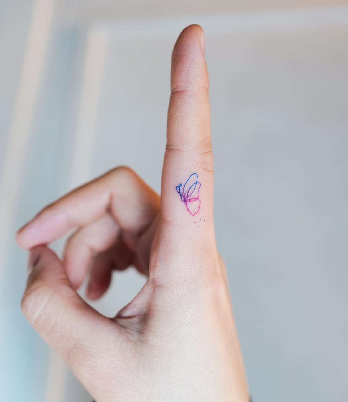 Tiny Colorful Butterfly Tattoo on the Side of Index Finger